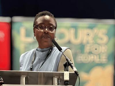 A woman with glasses speaks at a podium during a conference event