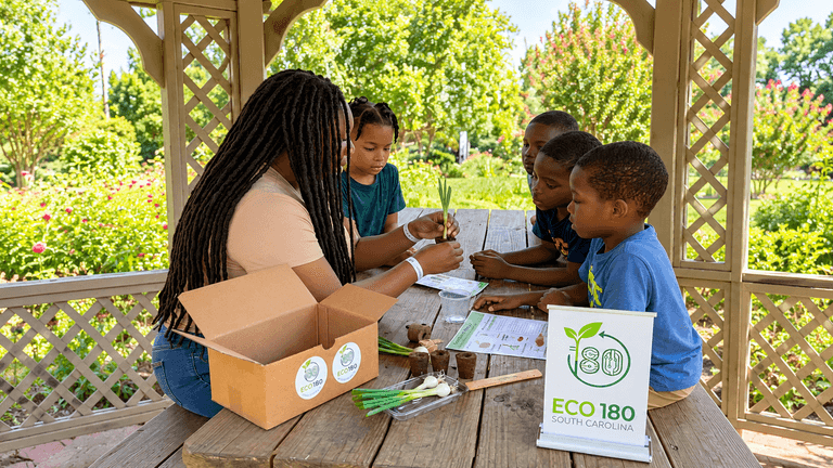 Children and an adult participate in a gardening activity at a gazebo.