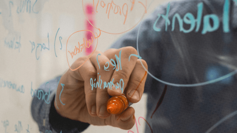 Person writing on a glass board with colorful markers and brainstorming ideas